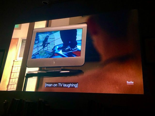 Over a shoulder we see an old TV on a metal cart - on screen is a caged parrot and a kid's legs on a gymnasium floor
