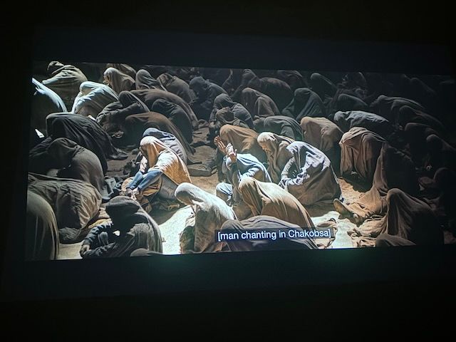 A crowd in desert robes, sitting cross-legged in prayer
