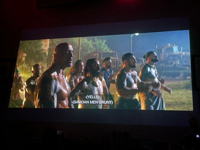 The Rock, shirtless, standing with a group of men at night in front of large equipment
