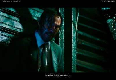 Keanu drenched in a suit and tie with his back to a metal wall and covered in dramatic shadows
