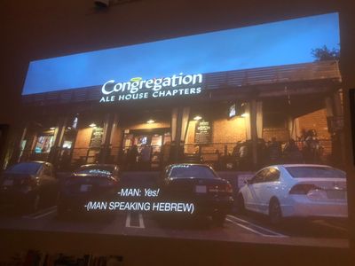 several cars parked in front of a Congregation Ale House Chapters with people eating on the patio - the sign has a halo over the first g, and horns on the second
